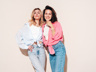 Fototapeta premium Two young beautiful smiling brunette and blond female in trendy summer clothes. Carefree women isolated, in studio. Positive models having fun. Cheerful and happy