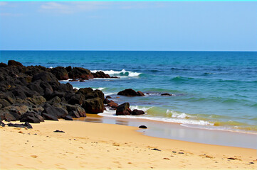 A sandy beach with rocks and waves crashing on the shore.