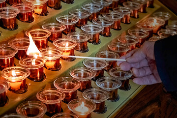 Candles burning in a church with hand visible lighting a candle