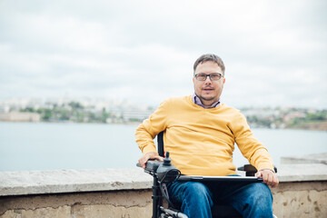Smiling young disabled man use phone on a wheelchair in a park at sunlight outdoors.