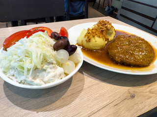 Hearty meal with salad, pickles, mashed potatoes, and meat patty in sauce