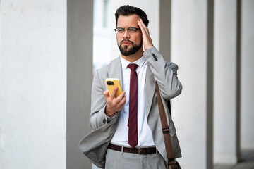 Stressed businessman having headache while reading bad news on smartphone