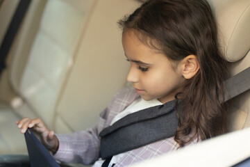Cute school-aged girl sitting in a car with her seatbelt fixed