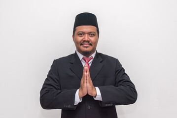 Smiling Indonesian Professional in Peci and Suit with a Respectful Welcoming Gesture