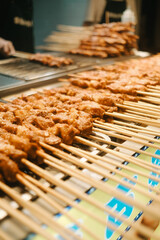 Close-up shot of freshly grilled meat skewers arranged in rows at a food market stall. Street food vendor preparing satay or Shao Kao skewers, showcasing delicious and smoky grilled cuisine.