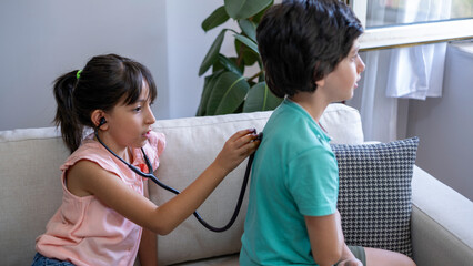 Two siblings are playing doctors. The girl is examining her brother with a stethoscope.