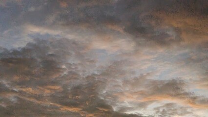 A dynamic sky full of textured clouds. The clouds are a dark gray and blue, with warm streaks of orange and pink from a distant sunrise, creating a dramatic, abstract, and colorful pattern.