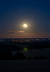 Bright Full Moon Shining in the Dark Night Sky Over a Distant Landscape.