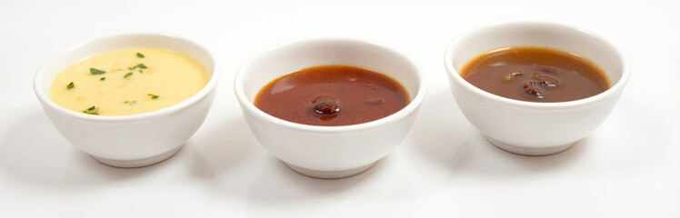 Three small white bowls filled with creamy, tangy, and savory sauces on white background