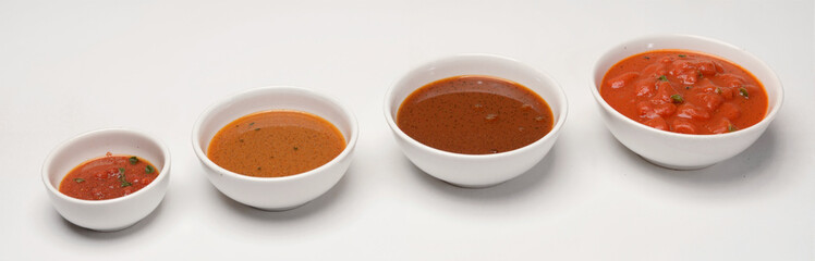 Four white bowls filled with different types of sauce, arranged in row on white background