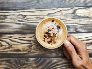 A person takes a fresh cup of coffee with cocoa granule as the topping. The combination of strong coffee, creamy flavor, smooth foam, and crunchy choco granule.