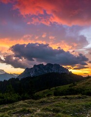 Obraz premium Vibrant sunset colors paint the sky above a silhouetted mountain range and rolling hills