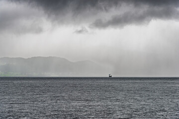A ferry moves steadily across the choppy sea as dark clouds gather, hinting at an approaching storm in the distance.