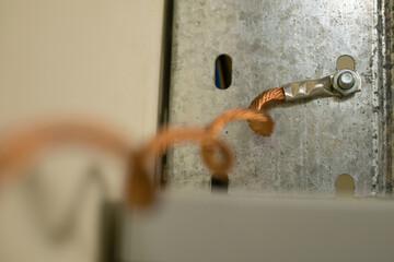 A twisted copper multi-strand grounding wire screwed with a nut to a galvanized cable tray