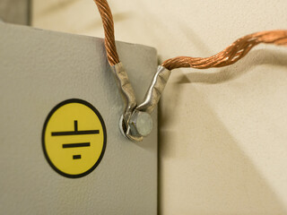 Close up of a copper multi-strand grounding wire screwed with a nut to a metal cabinet with a...
