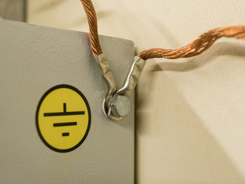 Close up of a copper multi-strand grounding wire screwed with a nut to a metal cabinet with a yellow "Grounding" label