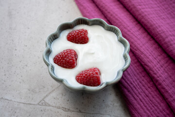 Porcelain bowl and natural yogurt with red berries on the stone marble table.
