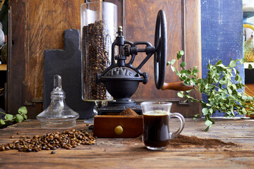 Glass cup of freshly brewed black coffee on a rustic wooden table with ground coffee, beans, and a...