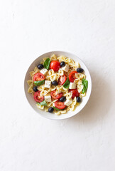 Pasta salad with farfalle, tomatoes, cheese, olives and basil. Italian cuisine. Vegetarian food.