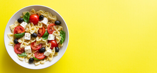 Pasta salad with farfalle, tomatoes, cheese, olives and basil. Italian cuisine. Vegetarian food.