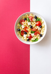 Pasta salad with farfalle, tomatoes, cheese, olives and basil. Italian cuisine. Vegetarian food.