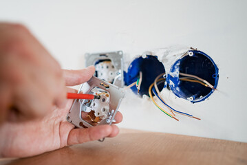 Electrician tightening screws on a new electrical socket during a home renovation project,...