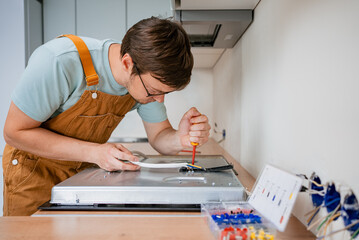 Electrician wearing brown overalls and glasses is using a screwdriver to connect wires to an...