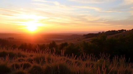 Obraz premium Sun setting over hills grass in foreground glows with light
