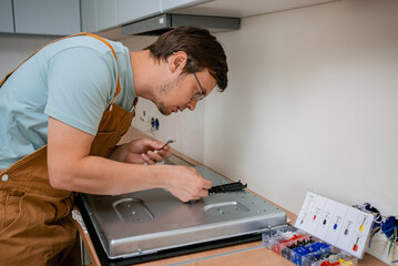 Electrician wearing brown overalls and glasses is carefully connecting wires to the back of a new...