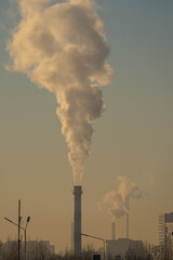 Smoke billowing from industrial chimneys against a dusky sky creates a hazy cityscape at sunset,...