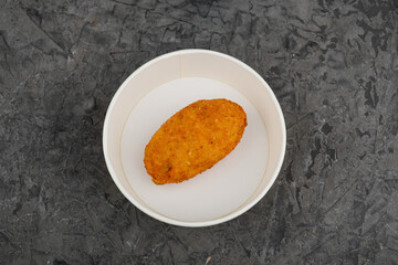breaded Kiev cutlet in a disposable plate on a gray concrete background