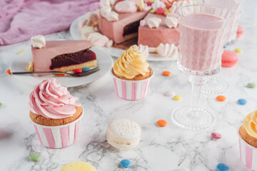 Close up of pink cake, marshmallows, candies, sweet cupcakes and milkshake on marble table