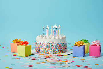 Delicious cake with candles, colorful gifts and confetti on blue background