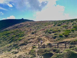 Mountain hiking trail with wooden fence, dry grass, and clear blue sky on a sunny day.