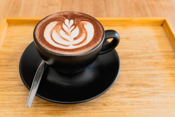 A steaming hot cup of frothy cappuccino sits on a wooden table, its rich brown tones and creamy white foam a perfect morning beverage
