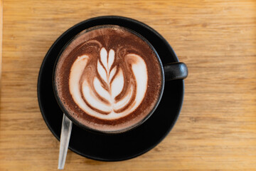 A delicious hot cup of cappuccino with chocolate art sits on a table