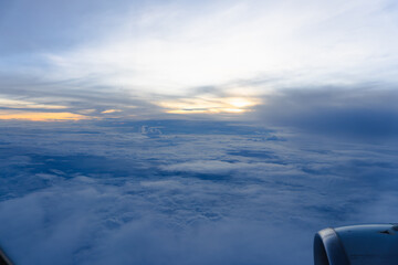 High above the clouds, a white airplane soars through a stunning blue sky at sunset
