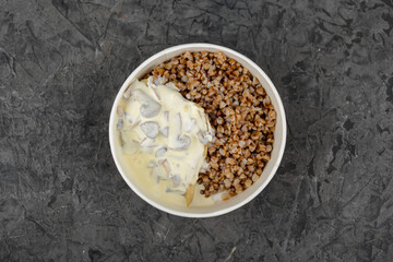 Buckwheat with mushrooms in a creamy sauce in a disposable plate on a gray background
