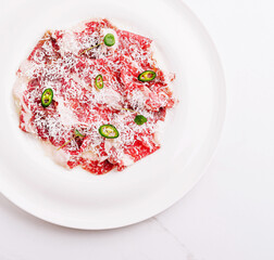 Delicious beef carpaccio with jalapenos and cheese served on a white plate