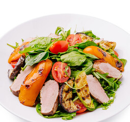 Colorful salad with grilled vegetables and sliced meat on a white plate