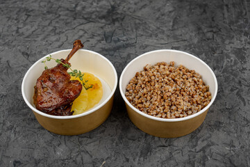 Duck leg and buckwheat porridge in a disposable plate on a gray background