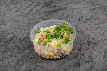 Olivier salad with green peas in a disposable plate on a gray concrete background