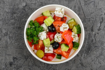 Greek salad in a disposable plate on a gray concrete background