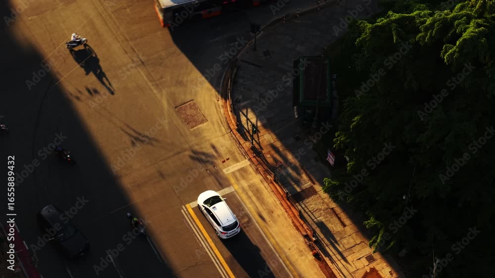 Poster drone makes a top-down orbit shot over a stopped car in genoa at golden hour, with a turning bus cas