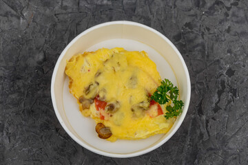 omelet with vegetables and mushrooms in a disposable plate on a gray background