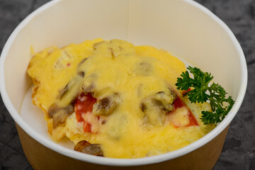 omelet with vegetables and mushrooms in a disposable plate on a gray background macro