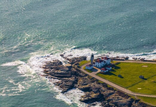 Aerial view of the iconic white and red roofed Beavertail Lighthouse standing proudly on the rugged coastline against the backdrop of the blue Atlantic ocean, Newport, Rhode Island, United States.