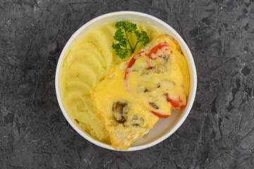 mashed potatoes and omelet with vegetables in a disposable plate on a gray concrete background