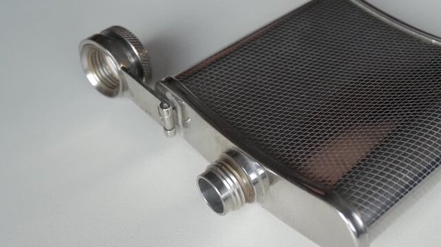 Close-up of metallic flask with textured design on white background, zoom out