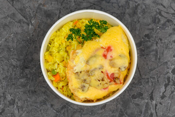 rice with vegetables and omelet with vegetables in a disposable plate on a gray background